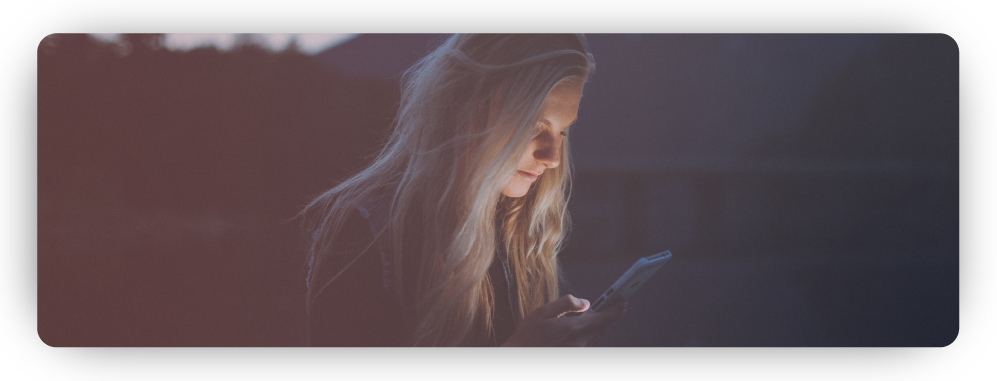 Young woman standing outdoors late at night by a lake looking anxiously at smartphone